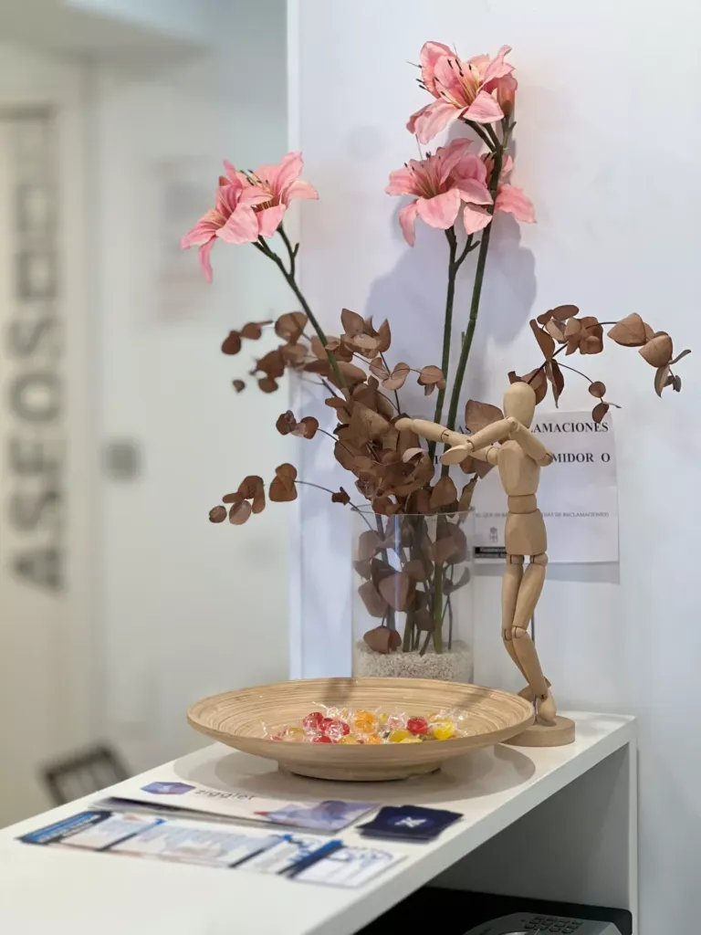 Jarrón con flores secas, plato de madera con caramelos y un muñeco de madera en el mostrador