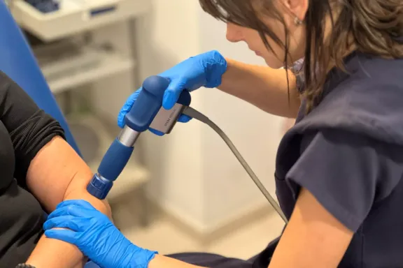 Fisioterapeuta realizando tratamiento de ondas de choque en el codo de una clienta