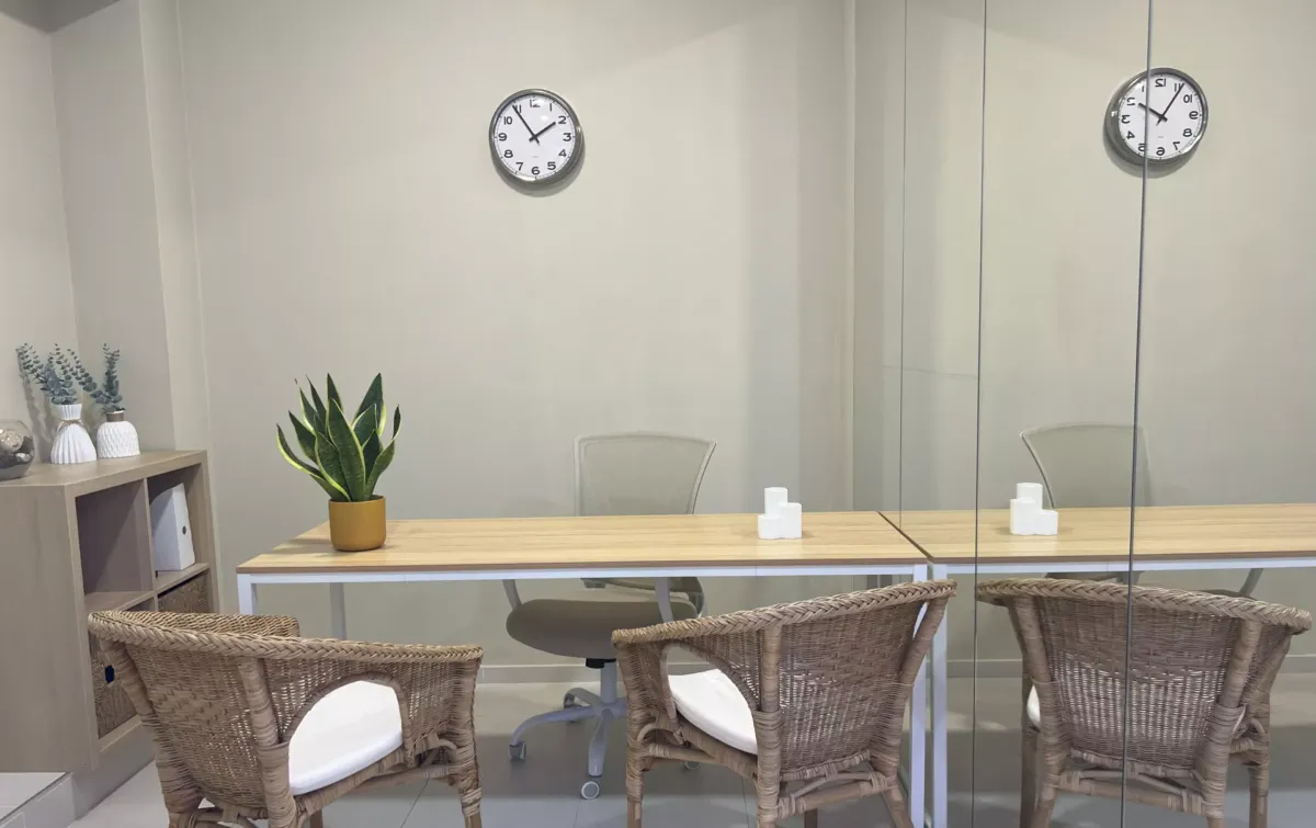 Sala para psicoterapia con mesa grandes, sillas, estantería, plantas y un reloj colgado en la pared